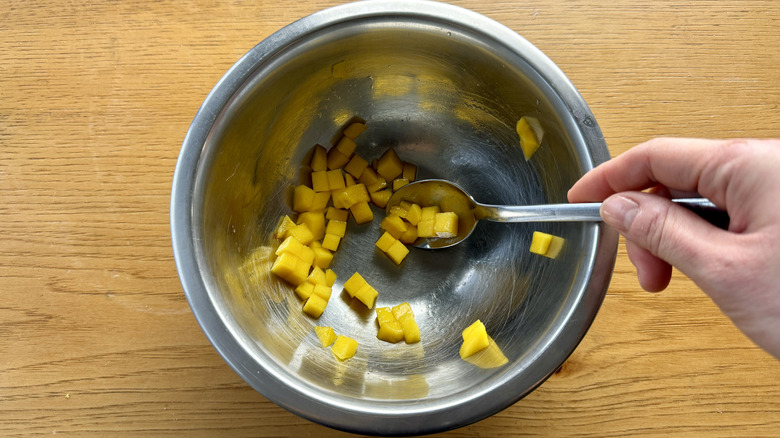 hand stirring mango pieces in a metal bowl