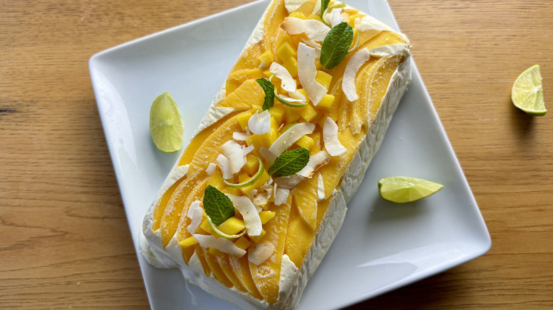 whipped cream graham cracker icebox cake with mango, lime wedges, mint leaves, and coconut