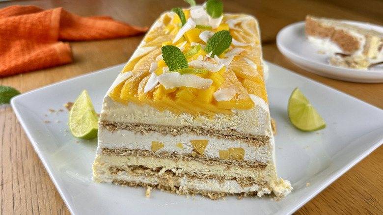 whipped cream graham cracker icebox cake with mango, lime wedges, mint leaves, and coconut