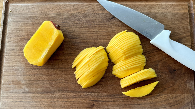 sliced mango with a large knife on a wooden board