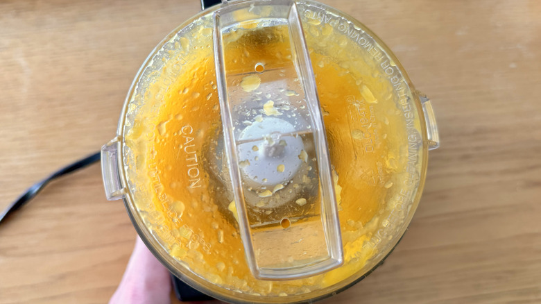 person's finger touching a food processor full of pureed mango