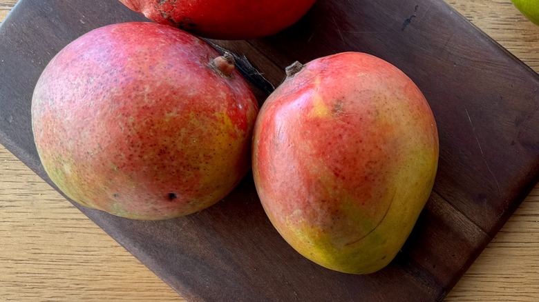 two whole mangoes on a wooden board