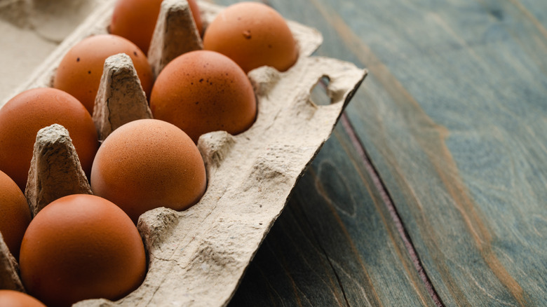 Brown eggs in a paper carton on a wooden background.