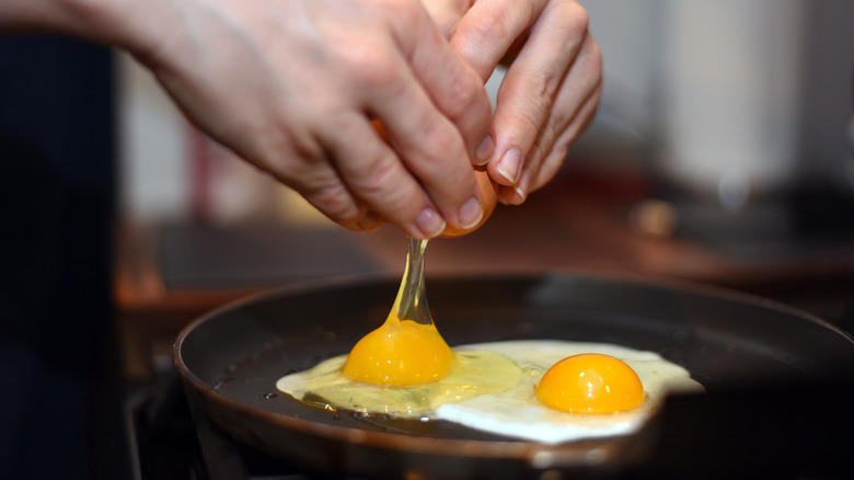 Person cracking an egg into a frying pan.