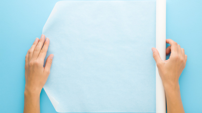 Person unrolling wax paper on blue table