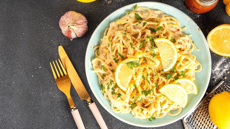 Plate of creamy spaghetti with sliced lemons and chopped herbs