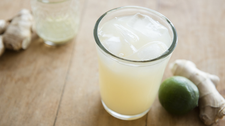 Glass of ginger ale rests next to lime and ginger roots on a table