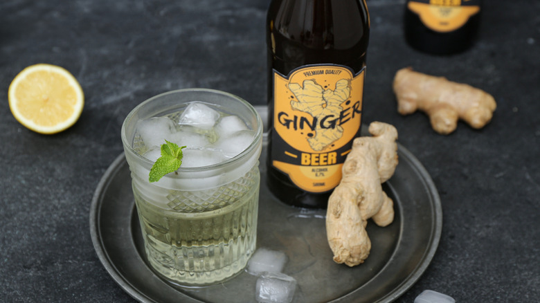 Ginger beer in a glass on a plate next to a bottle and ginger roots