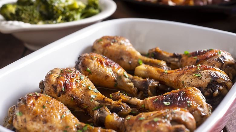 Marinated chicken legs in a baking dish with broccoli in background