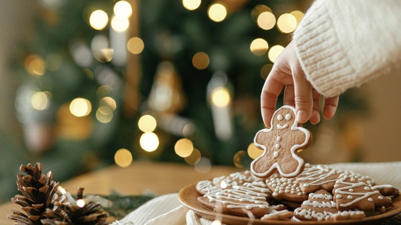 Person holding gingerbread man cookie with Christmas tree in background