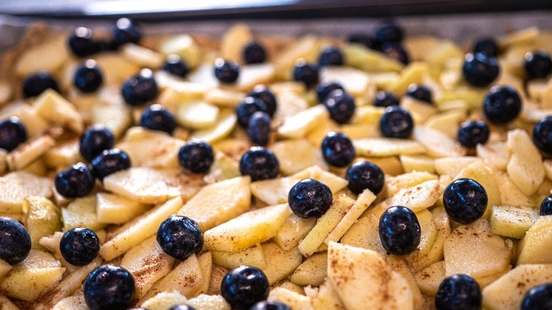 A slab pie of sliced apples and fresh blueberries is ready to be baked