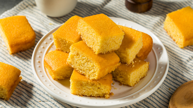 A pile of cornbread squares are arranged on a plate and table.