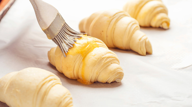 Egg wash being brushed onto unbaked croissants