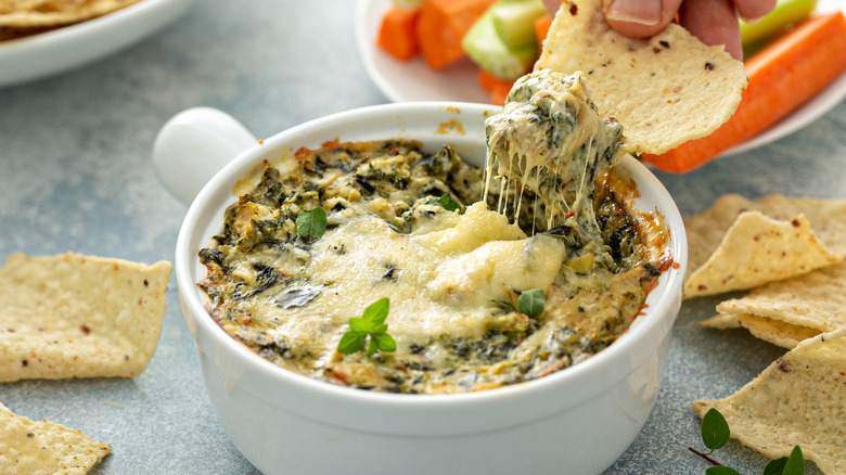 Bowl filled with spinach artichoke dip surrounded by tortilla chips