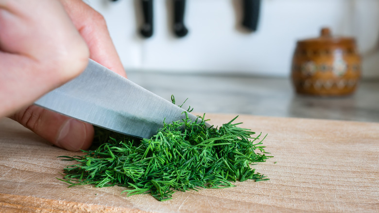 closeup of knife chopping fresh dill on a wooden cutting board