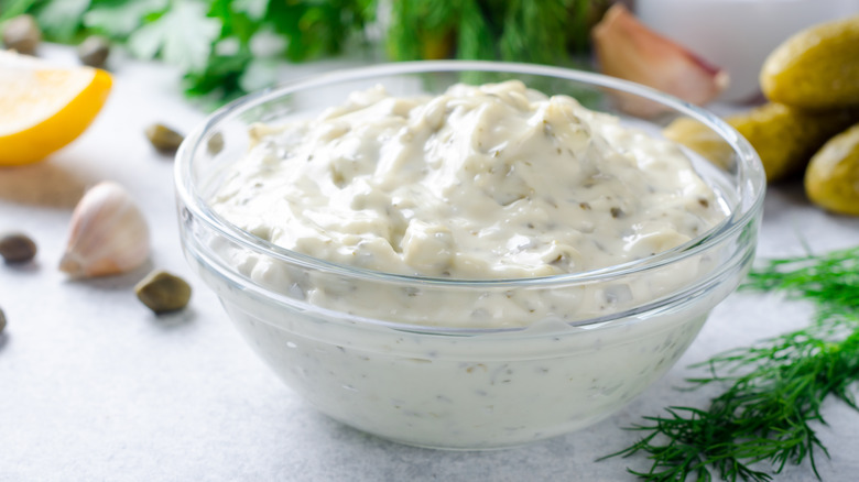 Bowl of tartar sauce with cut lemons and fresh herbs in the background