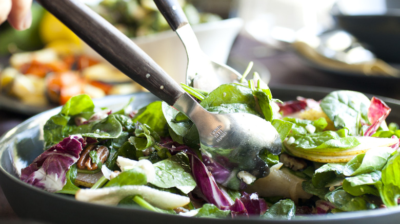 person using tongs in a green salad