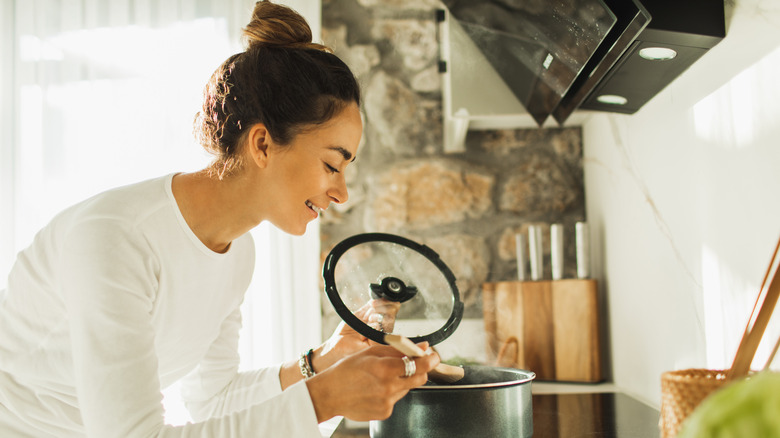 A person lifts a lid to peer into a saucepan on the stove