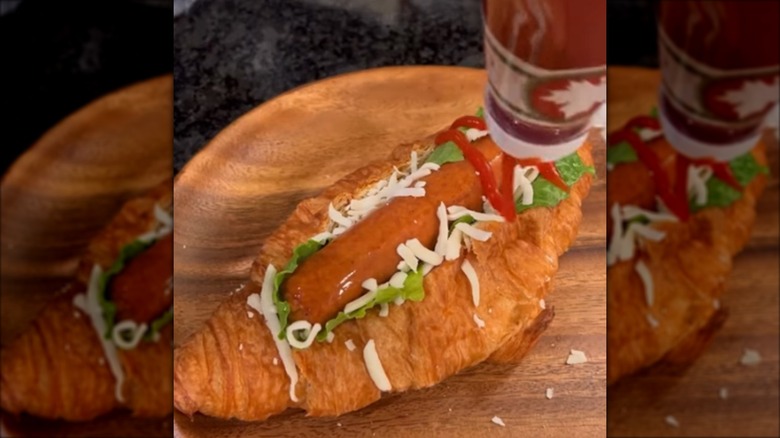 A croissant hot dog being topped with ketchup