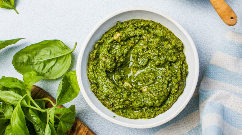 Pesto on white background surrounded by basil leaves and striped tea towel