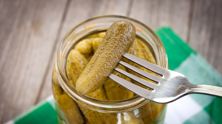 Fork holding up small pickle over jar