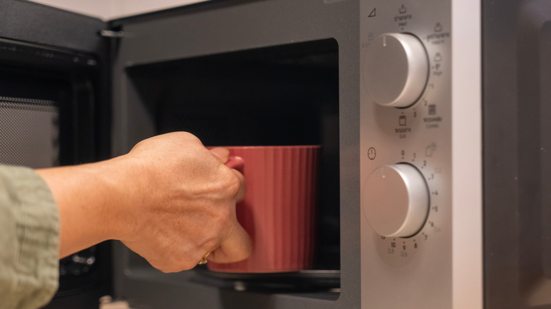 Hand placing red mug in microwave