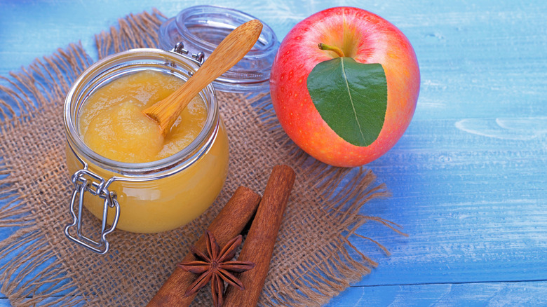 Homemade apple sauce in a glass jar next to cinnamon sticks and whole apple