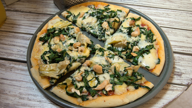 Pizza topped with artichokes, spinach, and nuts