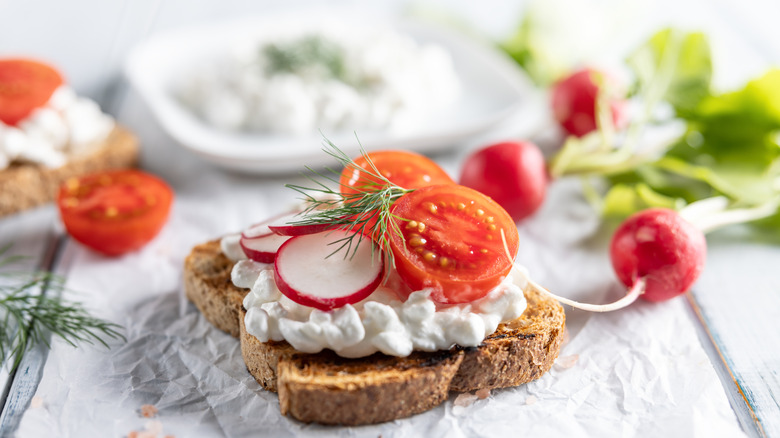 Cottage cheese sits on some toast and is topped with sliced tomato and radish and fresh dill