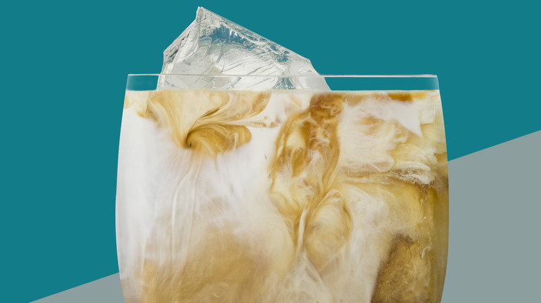 A white Russian cocktail in an ice-filled glass in front of a teal background.