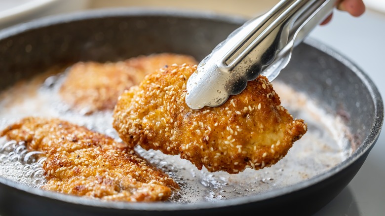 Three breaded chicken cutlets frying in a pan