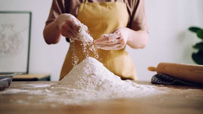 A baker mixes flour on a countertop with her hands