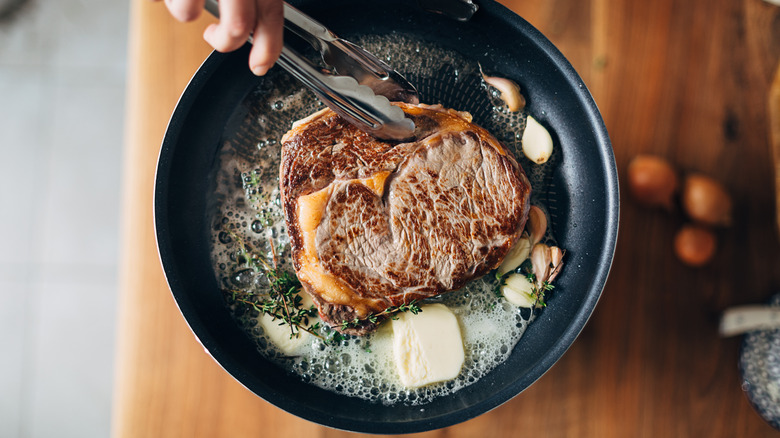Ribeye steak cooking in pan