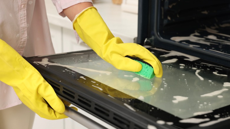 Person wearing yellow rubber gloves cleaning an oven