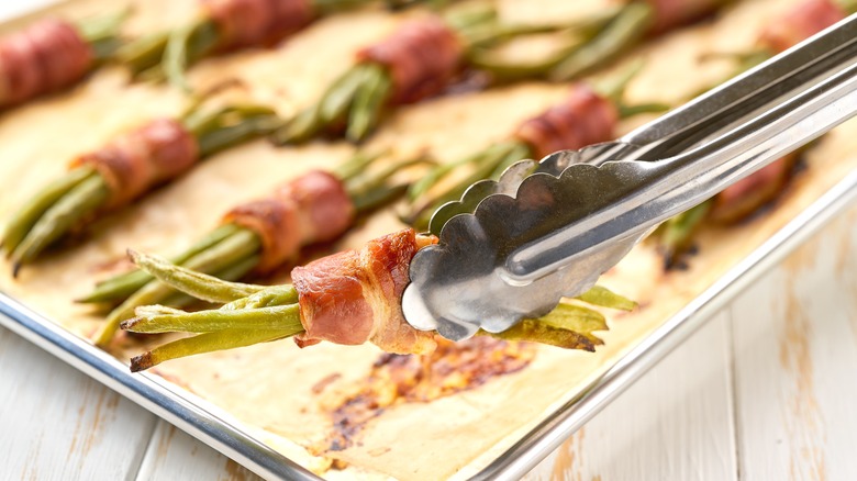 Tongs holding bacon-wrapped beans