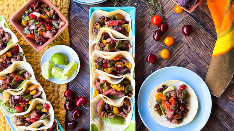 Grilled flank steak tacos with stone fruit salsa on serving dishes with garnishes