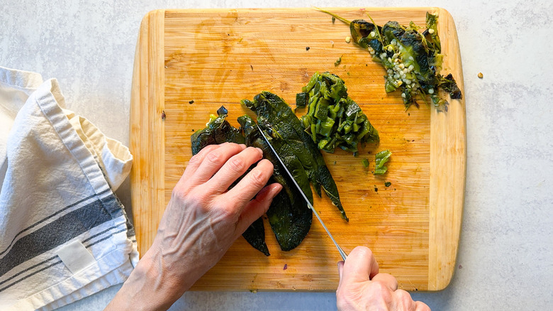 Chopping peeled and seeded grilled poblano peppers on cutting board with knife