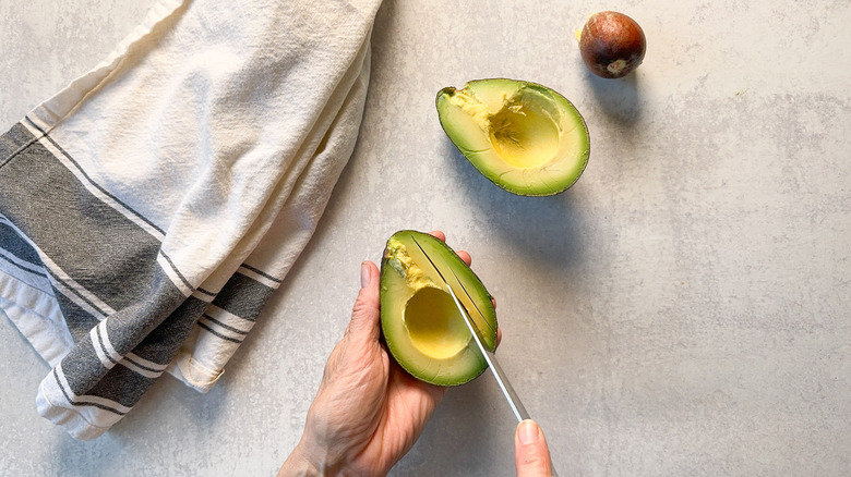 Slicing avocado in shell with knife  on countertop with towel
