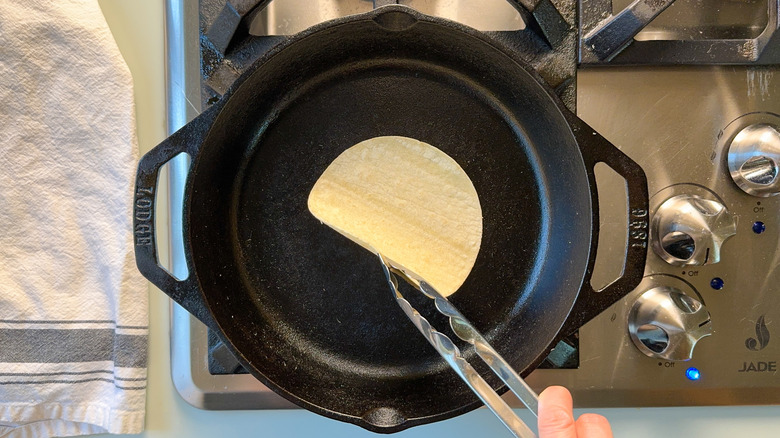 Warming corn tortillas in cast iron pan with tongs on stovetop