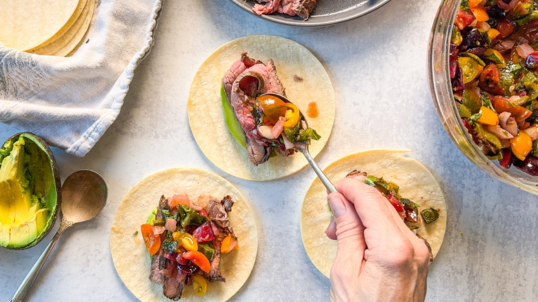 Assembling grilled flank steak tacos with stone fruit salsa on countertop