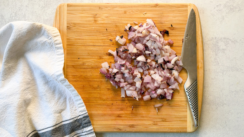 Chopped grilled onion on cutting board with knife and towel