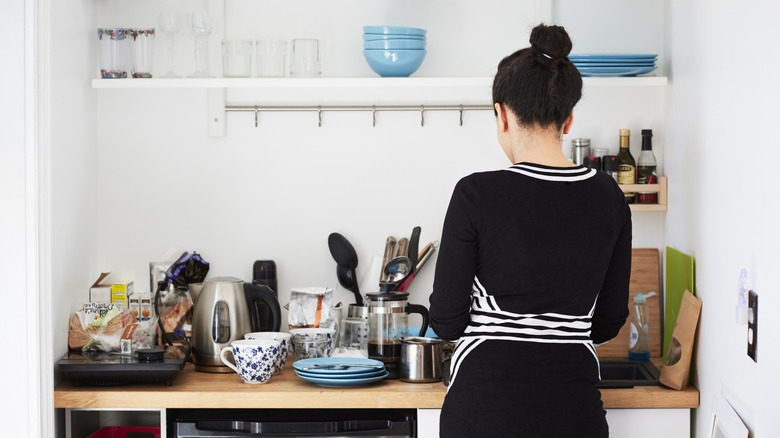 A person with their back to the camera at the counter of a small NYC apartment kitchen.