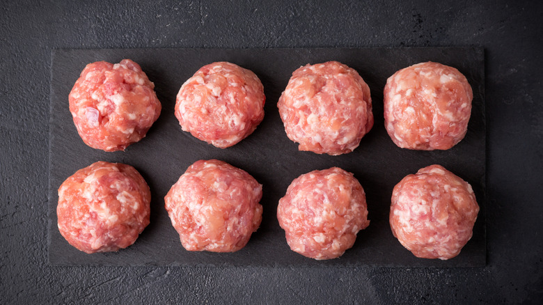 Eight raw turkey meatballs on black cutting board