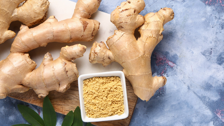 Fresh ginger root and a bowl of powdered ginger on the side