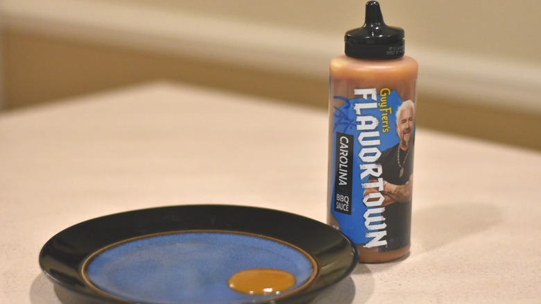 A bottle of Flavortown Carolina barbecue sauce next to a blue plate with a sample of gold sauce