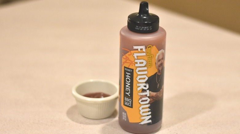 A bottle of Flavortown honey barbecue sauce next to a small white bowl with a sample of brown sauce