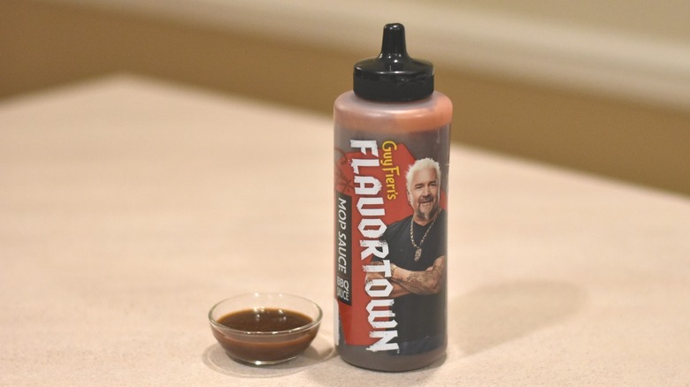 A bottle of Flavortown Mop Sauce barbecue sauce next to a small glass bowl with a sample of brown sauce