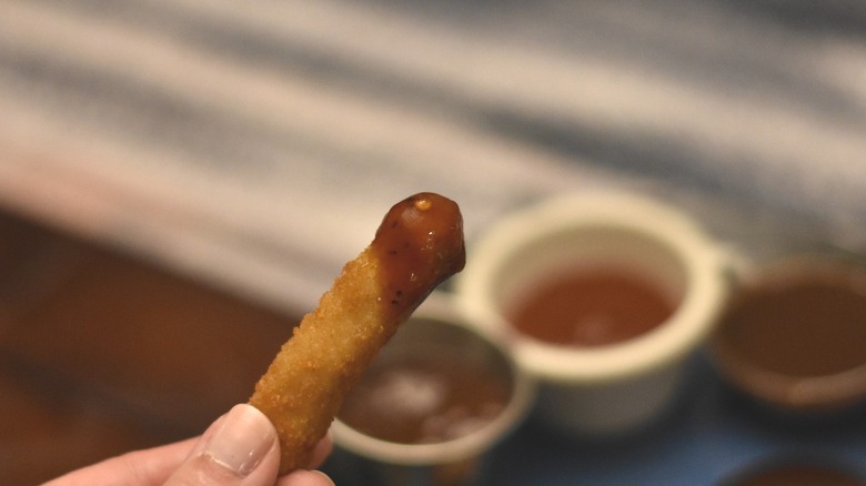 A chicken strip dipped in barbecue sauce in front of three samples of sauce in small bowls