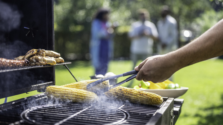 Hand turning corn on an outdoor grill