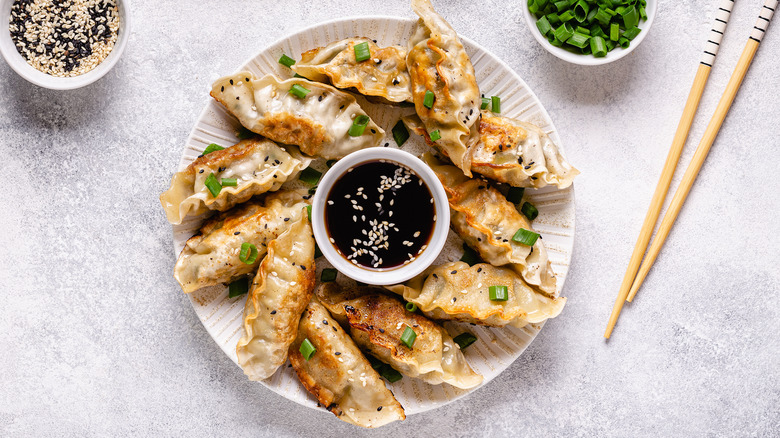 Gyoza arranged on a plate with soy sauce in middle.